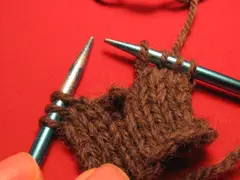 This photo shows the dropped stitch. Notice that right in the middle of the picture is a loop that has lost the yarn that is supposed to go through it. The yarn that has pulled out of this loop is lying behind the loop itself.