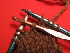 The dropped stitch has now been pulled through the loop forming a new loop. In this picture, the crochet hook has been thrust through the newly formed loop so that it won't be dropped again by accident.