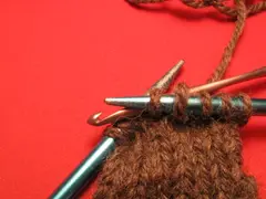 Finally, transfer the new loop (that is, the formerly dropped stitch) from the crochet hook to the knitting needle. In this photo, it was transferred to the right needle, but it should have been transferred to the left one instead.