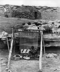 Though some people say the Navajo learned the art of weaving from the Pueblo people, the origins of Navajo weaving may never be known. The first Spaniards to visit the region wrote about seeing Navajo blankets. By the 18th century the Navajo had begun to import yarn with their favorite color, Bayeta red. Using an upright loom the Navajos made almost exclusively utilitarian blankets. Little patterning and few colors on almost all blankets, except for the much sought after Chief's Blanket, which developed from the 1st Phase, few wide bands, to the 2nd phase, wide bands with squares on the corners, to the 3rd Phase, which made more and more use of patterns and colors. Around the same time the Navajo people, who had long started traded for commercial wool, often from the uniforms of soldiers, rewove these into intricate multicolored blankets called Germantown.